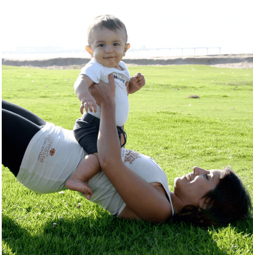 A young mother practices yoga in the grass with her baby.